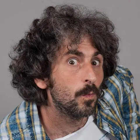 Alberto Farina, comico, con espressione sorpresa e camicia a quadri