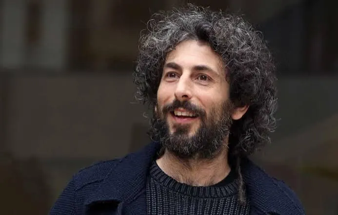 Ritratto di Alberto Farina, comico, con barba e capelli ricci, sorridente